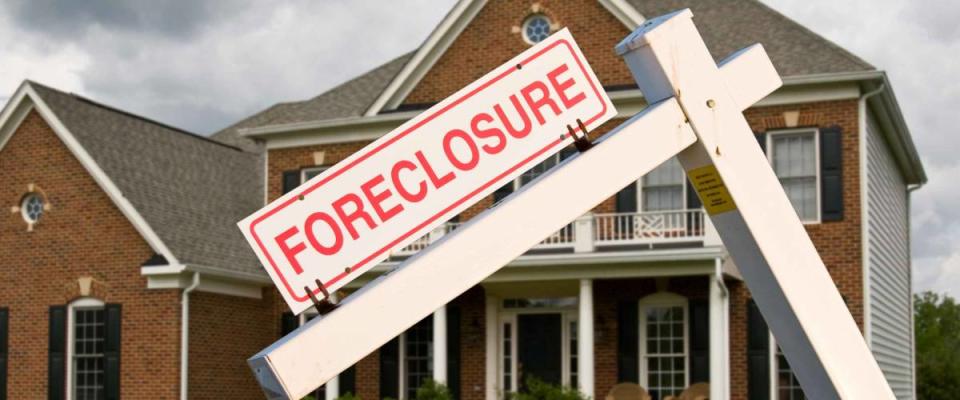 Leaning foreclosure sign in front of a modern single family home on a cloudy cold day