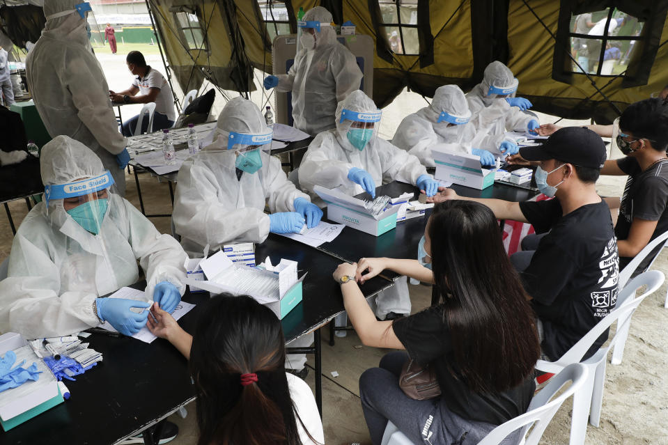 Health workers wear protective suits as they perform coronavirus rapid tests to people using the government's transportation assistance to return to their provinces, Tuesday, July 28, 2020 at a stadium in Manila, Philippines. Hundreds of people who were stuck in the capital due to travel restrictions during the lockdown stayed at a crowded stadium as they wait for free rides back to their provinces. (AP Photo/Aaron Favila)