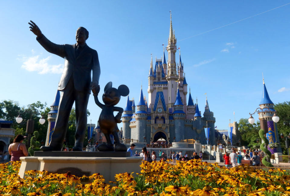 Statue of Walt Disney holding hands with Mickey Mouse in front of Cinderella's Castle in Disney World, visitors in the background