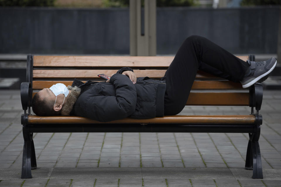 A man wearing a mask to help protect against the spread against the coronavirus naps on a bench at a park in Wuhan in central China's Hubei province on Friday, April 3, 2020. Chinese leaders are trying to revive the economy, but local officials under orders to prevent new infections are enforcing disease checks and other controls that add to financial losses and aggravation for millions of workers. (AP Photo/Ng Han Guan)