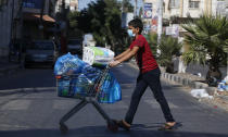 A Palestinian boy wears a face mask and gloves carries his shopping during a lockdown imposed following the discovery of coronavirus cases in the Gaza Strip, Thursday, Aug. 27, 2020. On Wednesday Gaza's Hamas rulers extended a full lockdown in the Palestinian enclave for three more days as coronavirus cases climbed after the detection this week of the first community transmissions of the virus in the densely populated, blockaded territory. (AP Photo/Hatem Moussa)