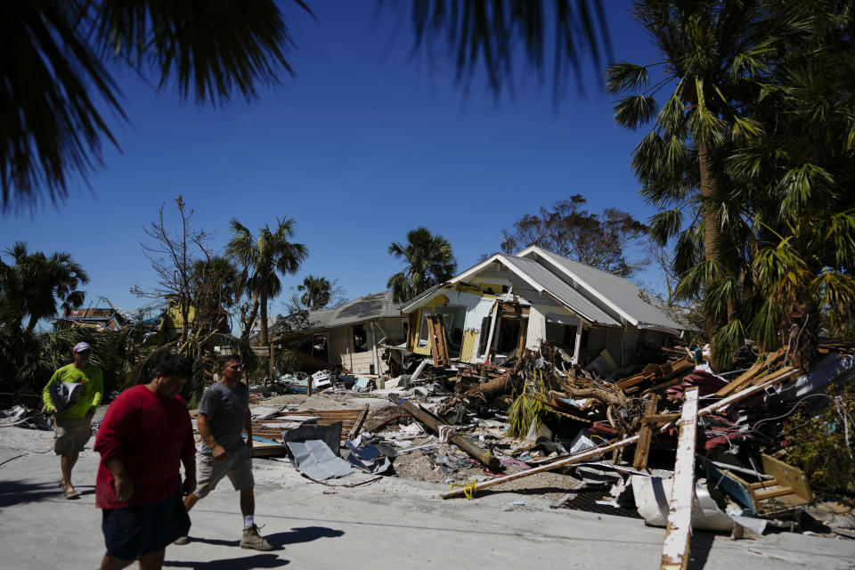 FILE - Men walk past destroyed homes and debris as they survey damage to other properties, two days after the passage of Hurricane Ian, in Fort Myers Beach, Fla., on Sept. 30, 2022. Florida's home insurance market was already on shaky ground. It now faces an even mightier struggle after the damage caused by the hurricane. (AP Photo/Rebecca Blackwell, File)