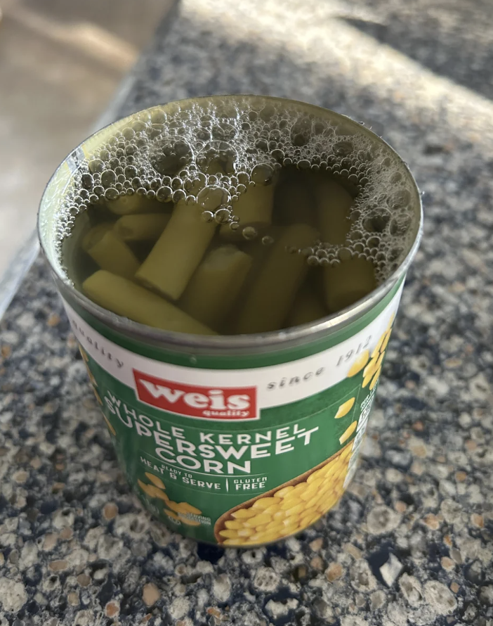 Opened can of green beans with bubbles on top, on a countertop