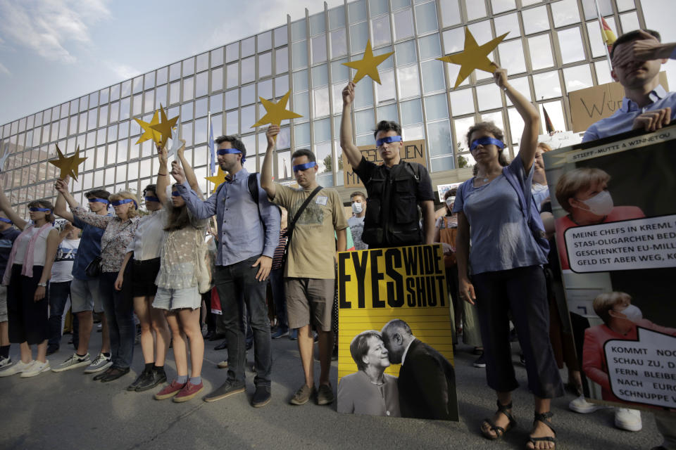 Protesters hold EU stars and keep their eyes closed behind a poster showing German Chancellor Angela Merkel and Bulgarian Prime Minister Boyko Borissov in front of the German Embassy in Sofia, Bulgaria, Wednesday, Aug. 12, 2020. Several hundred anti-government protesters gathered in front of Germany’s embassy in Sofia, calling on Berlin and Brussels to “open their eyes” to widespread corruption in Bulgaria. During the peaceful protest, dubbed “Eyes Wide Shut,” organizers complained that the European Union has willfully ignored the state of affairs in its poorest member state. (AP Photo/Valentina Petrova)