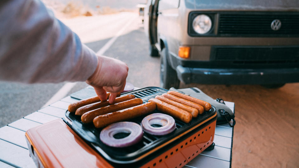 Person cooking hotdogs and onions on Eureka SPRK Camp Grill