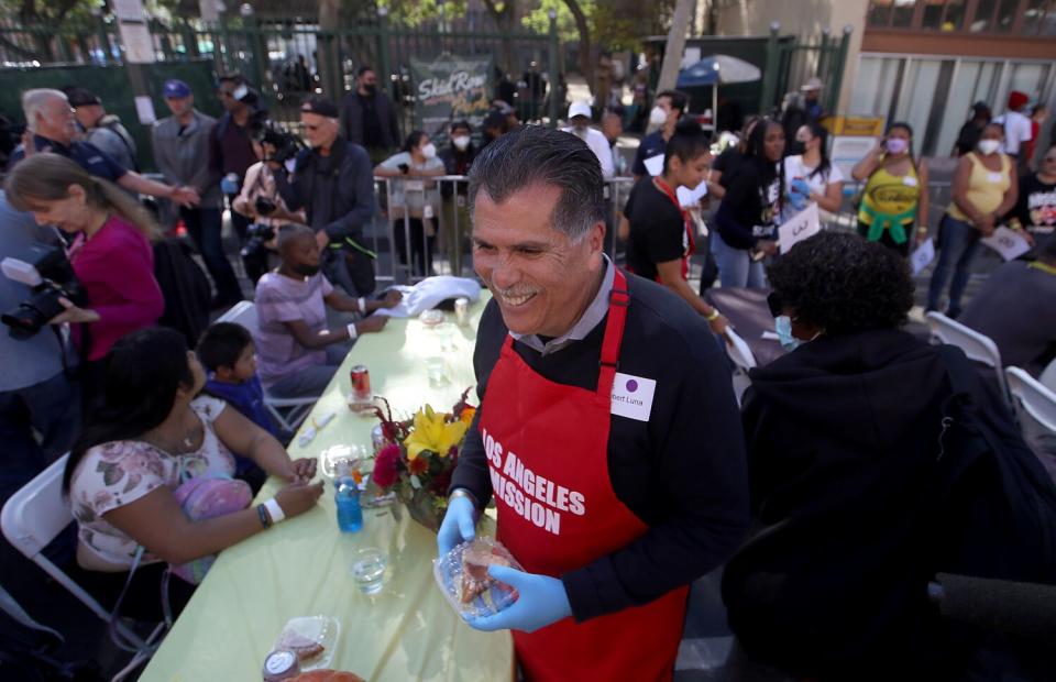 A smiling man holds a pie in a container among long tables outdoors.