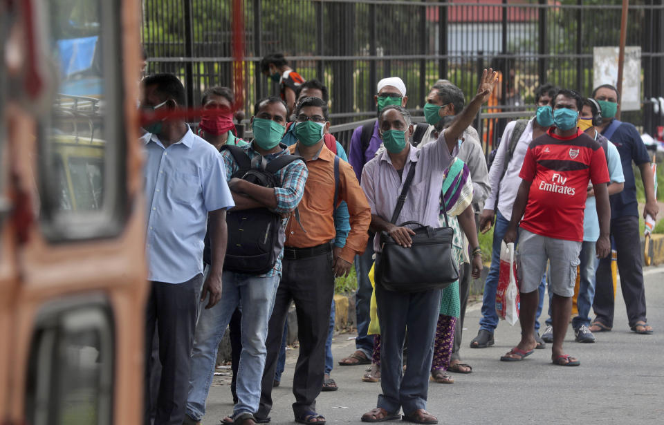 A man gestures to the driver of a bus as people wearing masks wait at a bus stop in Mumbai, India, Wednesday, July 22, 2020. With a surge in coronavirus cases in the past few weeks, state governments in India have been ordering focused lockdowns in high-risk areas to slow down the spread of infections. (AP Photo/Rafiq Maqbool)