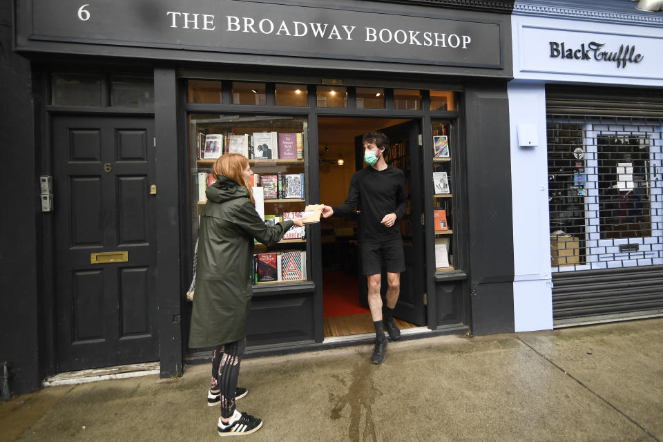 Tom, shop manager of Broadway Bookshop, hands off a book order to a customer outside the shop in Broadway Market, Hackney, in east London on June 18, 2020. The business started a website in June and converted to collect and delivery to cope with the lockdown measures due to the coronavirus outbreak. (AP Photo/Alberto Pezzali)
