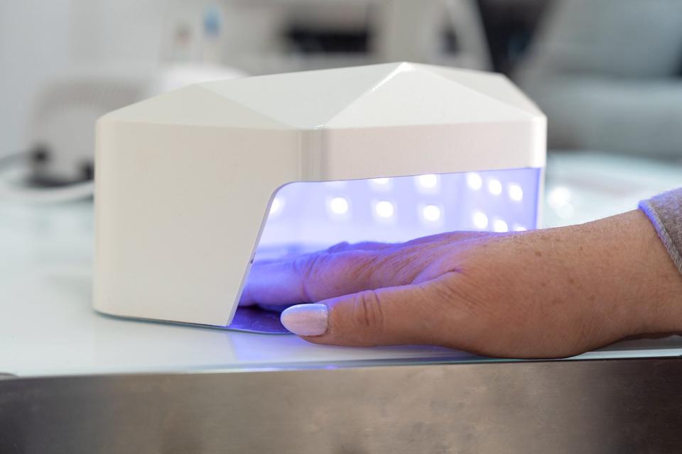 Close-up of a hand of an older woman drying her nails in an ultraviolet lamp