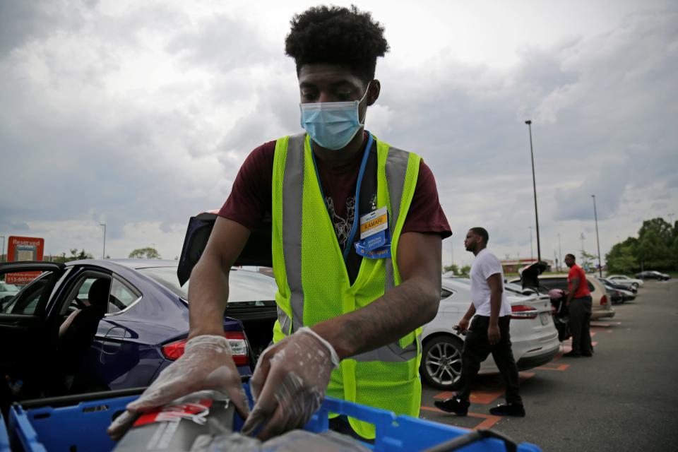 Personal shopper Kamari Barrow loads a customer's order into their car in the curbside pickup section of the parking lot at the Walmart Super Center in the Westwood neighborhood of Cincinnati on  Sunday, May 17, 2020.