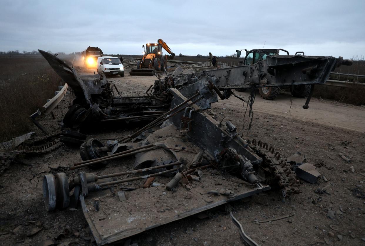 Cars and trucks drive past a destroyed military vehicle on the road in Ukraine's Kherson region.