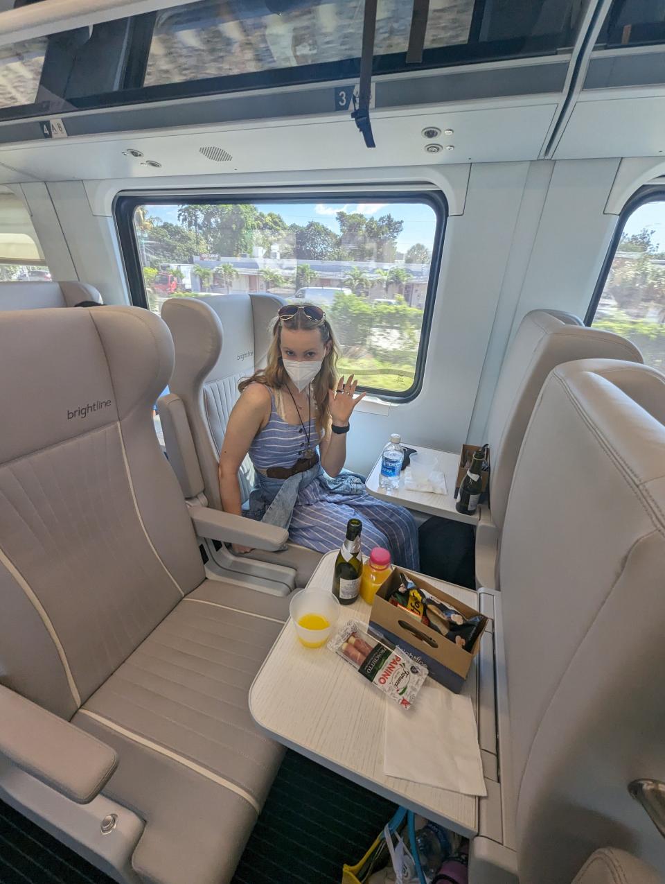 The writer is shown sitting in a premium seat on a Brightline train with snacks on. a small table in front of her.