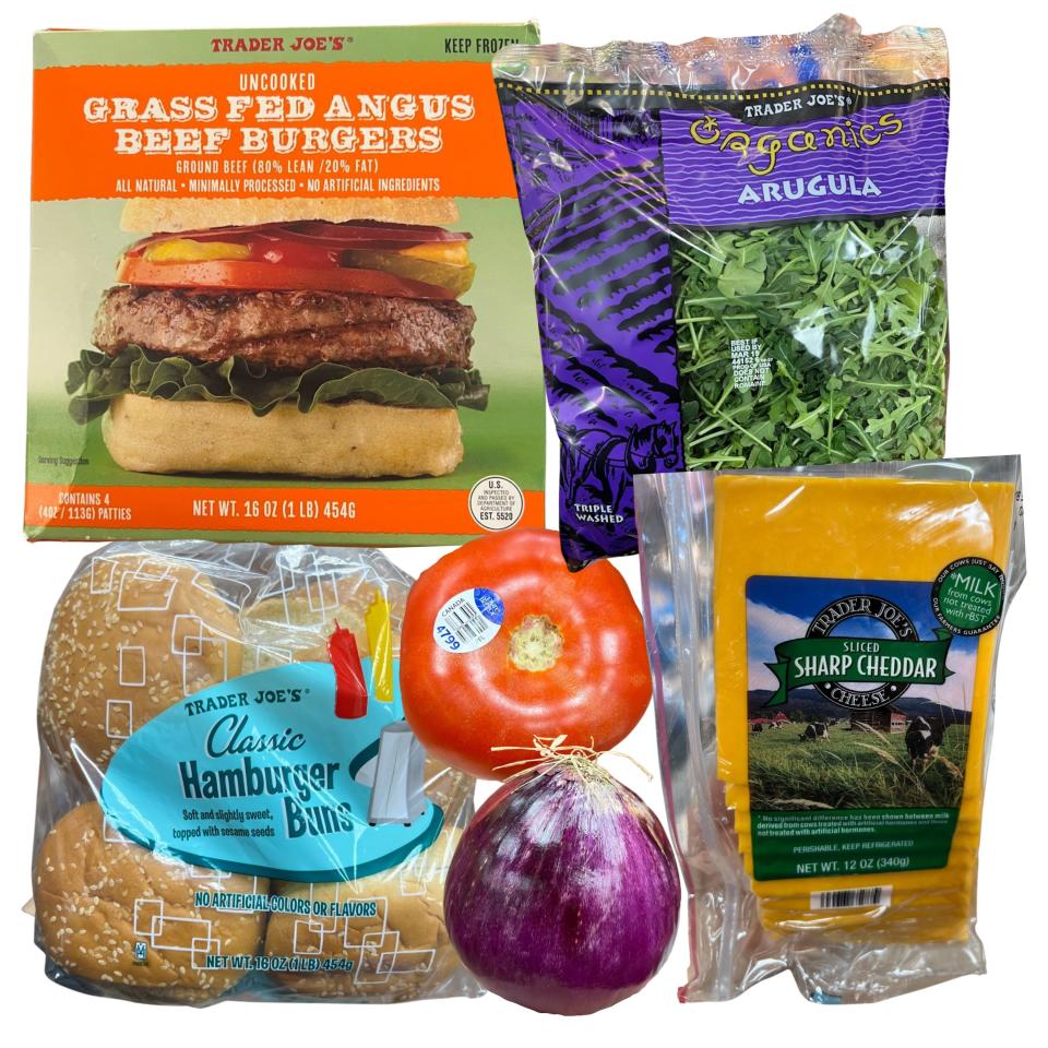 Grass-fed burgers patties in box, arugula in package, packaged slices of cheese, hamburger buns, onion, and tomato