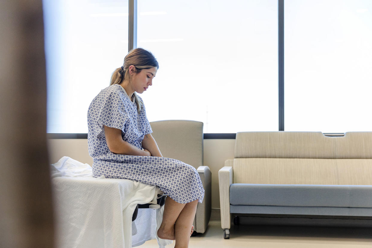 The anxious, sad, young female patient wears her gown as she waits in the hospital room Getty Images/SDI Productions