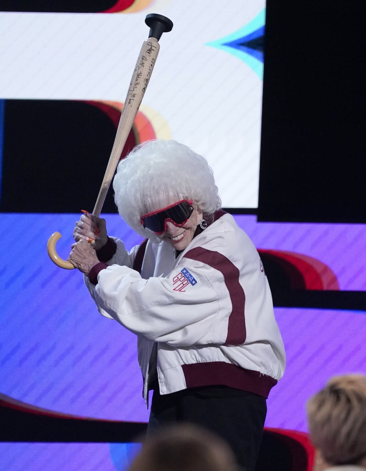 A smiling Maybelle Blair stands as if at bat with her baseball bat-shaped cane while onstage at the ESPY Awards