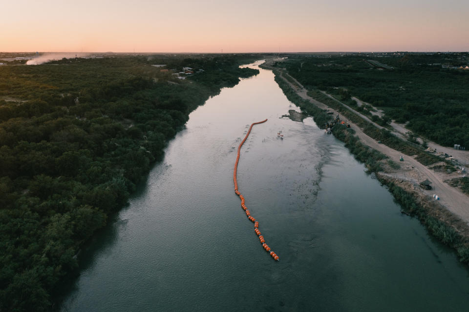 From above, string of orange buoys can be seen stretching along center of a river.