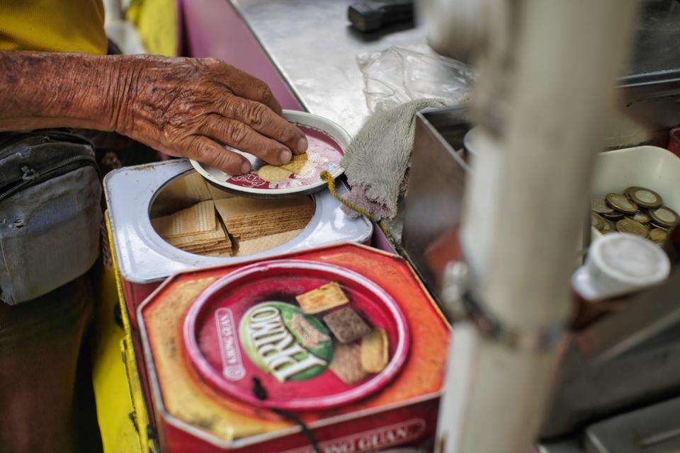 A close-up shot of an elderly man's wrinkled hands on the lid of a biscuit tin.