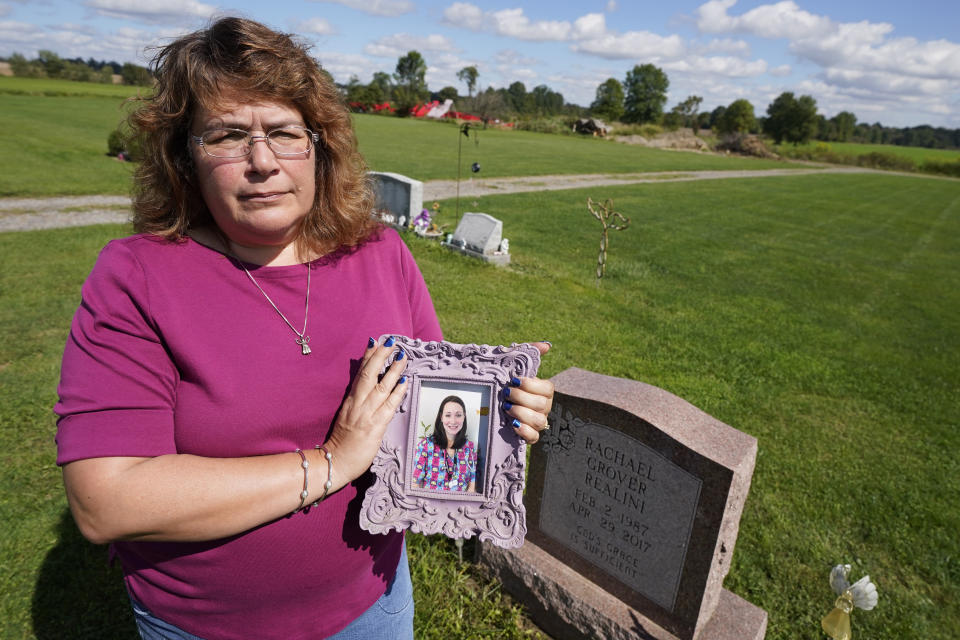 Sharon Grover holds a photograph of her daughter, Rachael, over the gravesite at Fairview Cemetery, Tuesday, Sept. 28, 2021, in Mesopotamia, Ohio. Grover believes her daughter started using prescription painkillers around 2013 but missed any signs of her addiction as her daughter, the oldest of five children, remained distanced. (AP Photo/Tony Dejak)