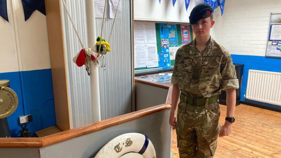 A boy in uniform standing by a mast