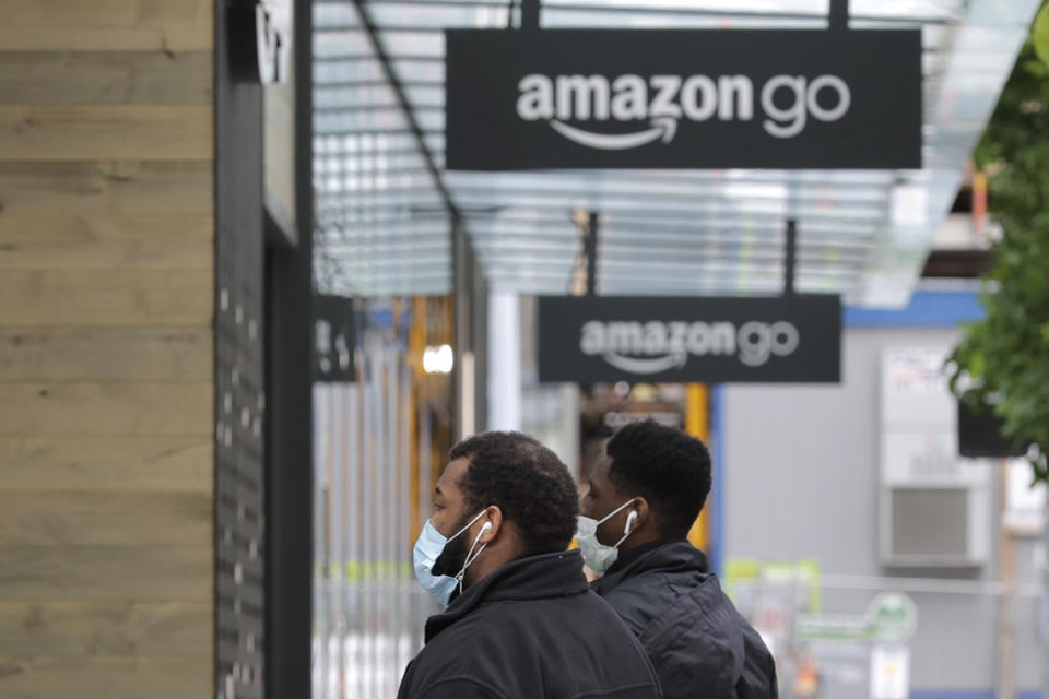 Two people wearing masks walk near an Amazon Go store, Thursday, April 30, 2020, in downtown Seattle. Amazon.com is expected to announce earnings for the first quarter of 2020 at the close of markets Thursday, a report that is expected to be closely watched due to the effects of the coronavirus outbreak on the company. (AP Photo/Ted S. Warren)