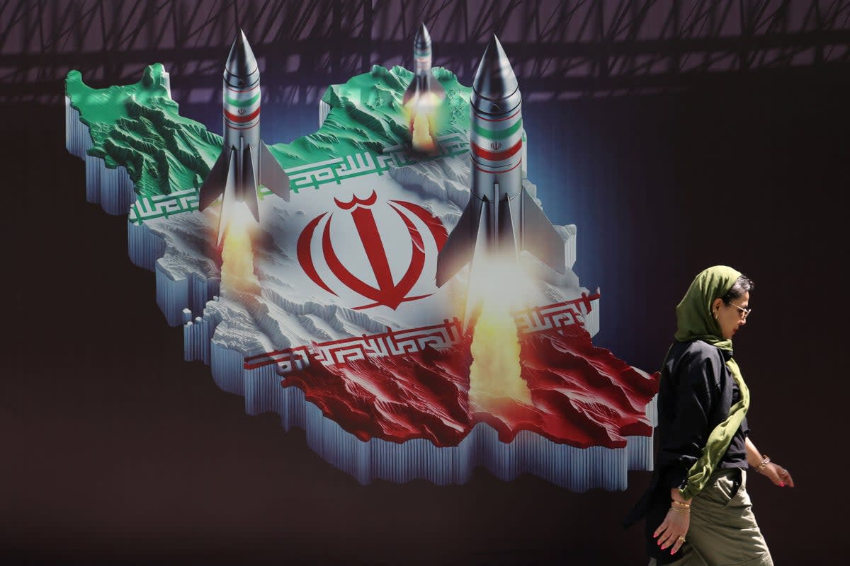 An Iranian woman walks past an anti-Israel banner with a picture of Iranian missiles on a street in Tehran (Reuters)