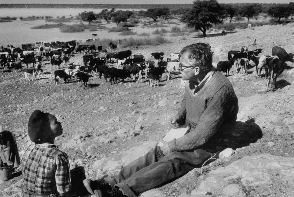 Author, Alan Paton (R) interviewing Herrero woman, Katrina Whiteman against the backdrop of the Tshani well during during his Kalahari expedition in Bechuanaland.