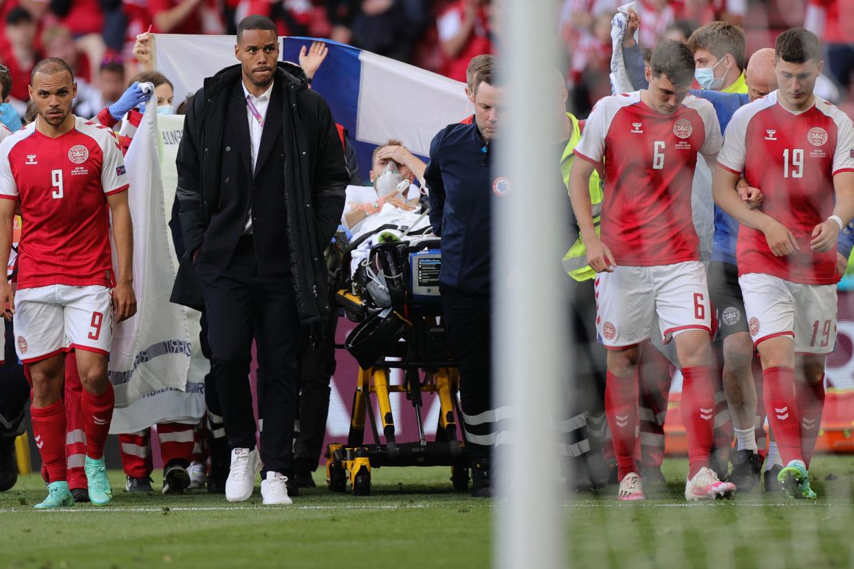 Denmark's players escort midfielder Christian Eriksen off the field after Eriksen collapsed on the pitch. (Photo by Friedemann Vogel / AFP via Getty Images)