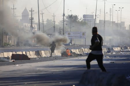 A man runs near burning objects at a protest during a curfew, three days after the nationwide anti-government protests turned violent, in Baghdad