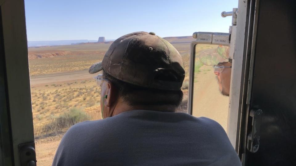 In this Aug. 20, 2019, image, train operator Ron Little is reflected in the rear view mirror as he leans out the window to get a better look at the mile-long coal train as it leaves the Navajo Generating Station near Page, Ariz. The power plant will close before the year ends, upending the lives of hundreds of mostly Native American workers who mined coal, loaded it and played a part in producing electricity that powered the American Southwest. (AP Photo/Susan Montoya Bryan)
