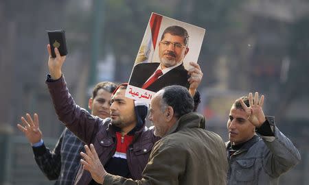 Supporters of the Muslim Brotherhood and ousted Egyptian President Mohamed Mursi hold a copy of the Koran and Mursi's picture at Talaat Harb Square, in Cairo, January 25, 2015. REUTERS/Mohamed Abd El Ghany