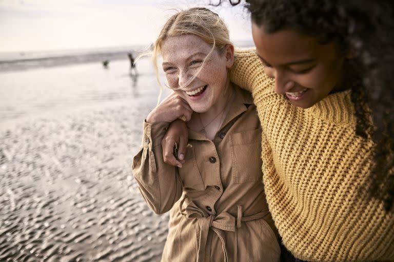 two smiling women walking arm in arm by the water