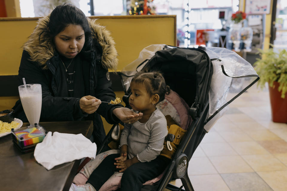 Grisy Oropeza, quien sigue confundida sobre si su familia obtendrá el asilo o sufrirá la deportación, alimenta a su hija menor, en un restaurante en Nueva York, el 27 de diciembre de 2023. (José A. Alvarado Jr./The New York Times)
