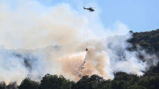 A helicopter drops water over trees during a wildfire near Cernon in the Jura region in central eastern France on August 11, 2022. (Photo by Jean-Philippe KSIAZEK / AFP)