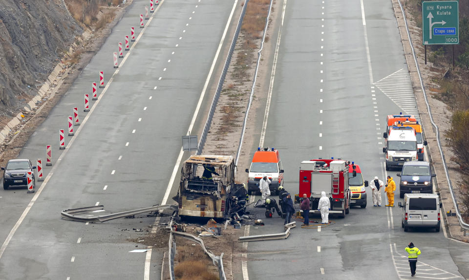 Firefighters and forensic workers inspect the scene of a bus crash on a highway near the village of Bosnek, western Bulgaria, Tuesday, Nov. 23, 2021. A bus carrying tourists back to North Macedonia crashed and caught fire in western Bulgaria early Tuesday, killing at least 45 people, including a dozen children, authorities said. (Minko Chernev/BTA Agency Bulgaria via AP)