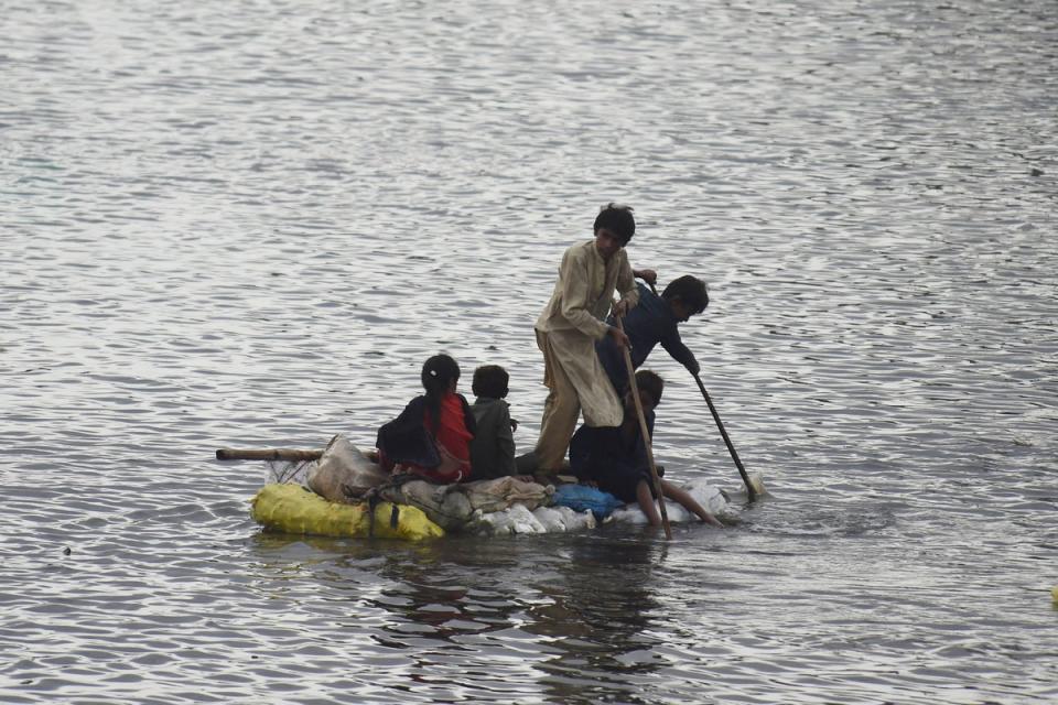 Children use a raft to make their way in a flooded area after heavy monsoon rains on the outskirts of Sukkur, Sindh province, on 27 August, 2022 (AFP via Getty Images)