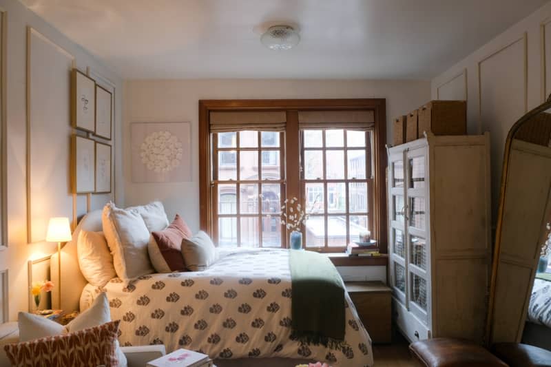 White bedroom with wainscoted walls, vintage furniture, and wood window trim