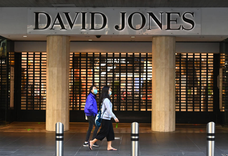 People wearing face masks walk in front of a closed David Jones store in an empty Bourke Street Mall in Melbourne.