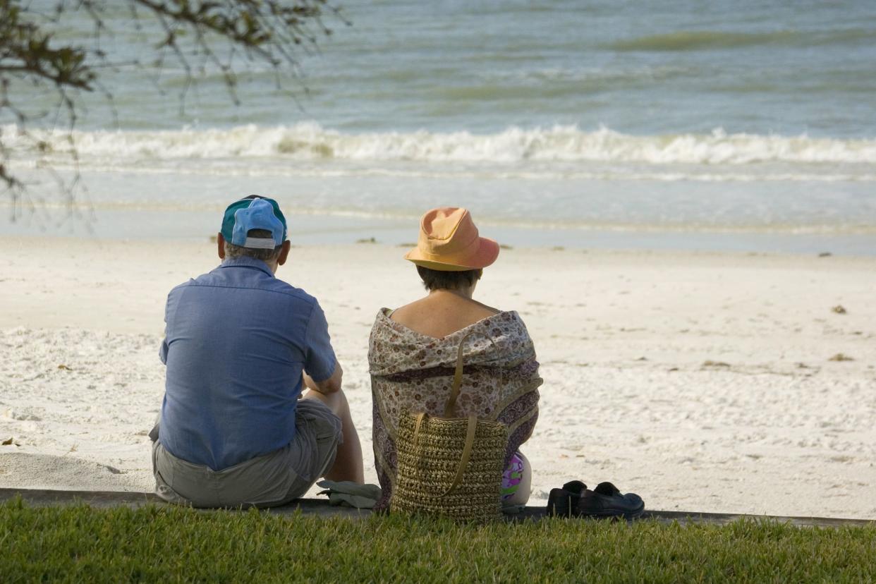 older sad couple sit on beach