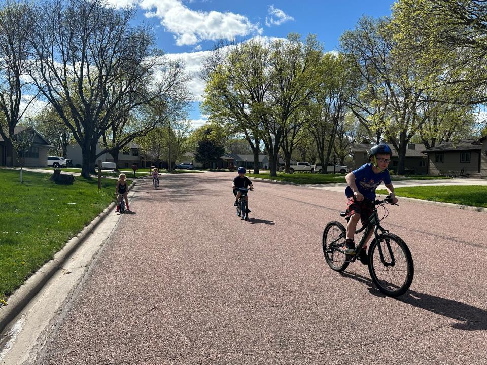 Four kids riding bicycles down a street on a sunny day.