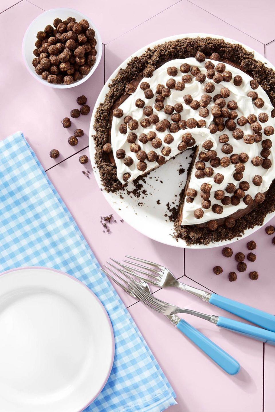 cocoa puffs and banana pie in a white pie dish with whipped cream and cocoa puffs on top with a slice removed