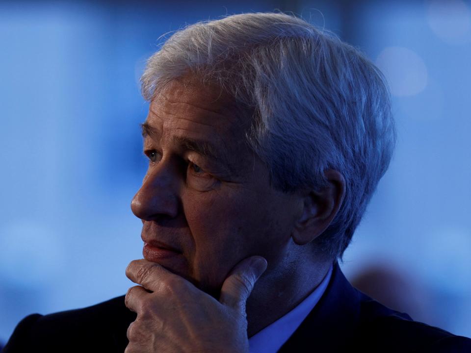 JPMorgan CEO Jamie Dimon holds his hand up to his chin in front of a blue background.