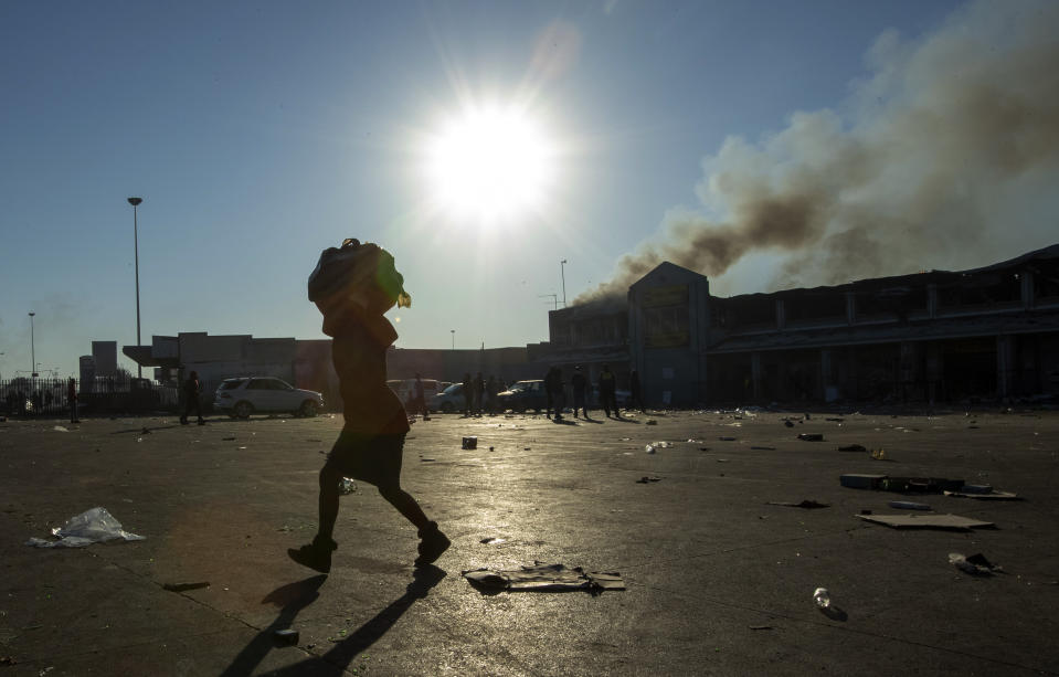 A woman carrying groceries looted from a nearby shop on her head at Naledi shopping complex in Vosloorus, east of Johannesburg, South Africa, Monday, July 12, 2021. Police say six people are dead and more than 200 have been arrested amid escalating violence during rioting that broke out following the imprisonment of South Africa's former President Jacob Zuma. (AP Photo/Themba Hadebe)