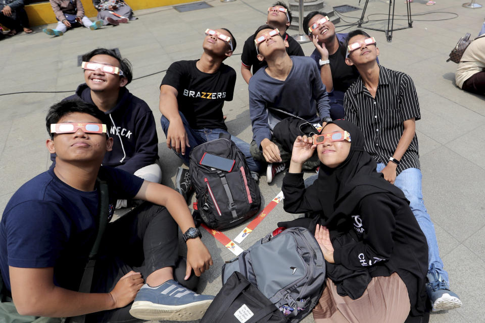 People look up at the sun wearing protective glasses to watch a solar eclipse in Jakarta, Indonesia, Thursday, Dec. 26, 2019. (AP Photo/Tatan Syuflana)
