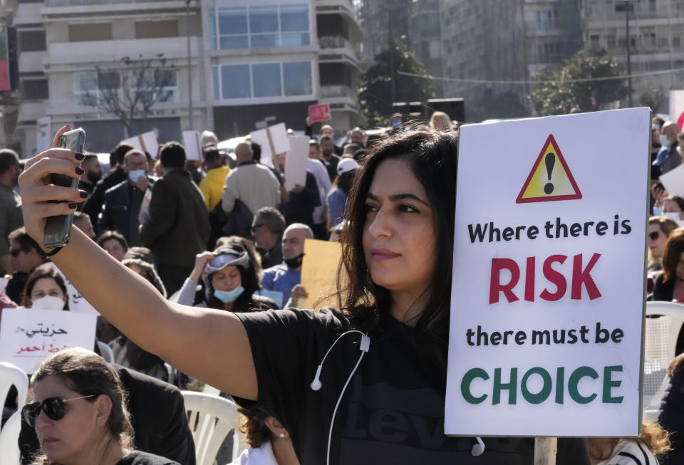 A protester takes selfie as she holds a placard during a rally to protest measures imposed against people who are not vaccinated, in Beirut, Lebanon, Saturday, Jan. 8, 2022. Vaccination is not compulsory in Lebanon but in recent days authorities have become more strict in dealing with people who are not inoculated or don’t carry a negative PCR test. (AP Photo/Hussein Malla)