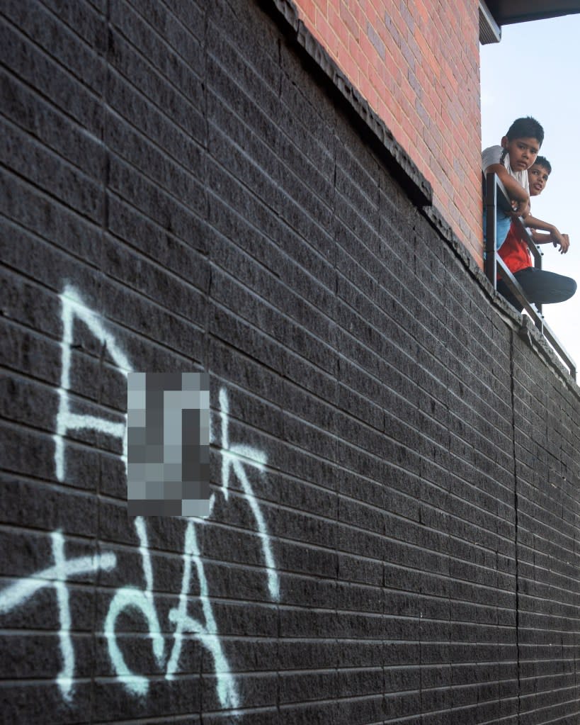 Two boys stand on the balcony of an apartment where anti-Tren de Aragua spray paint can be seen on the brick wall of the building. Jeremy Sparig