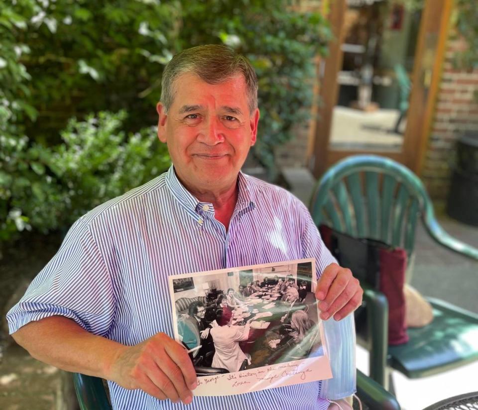 George Raya is pictured on Thursday, June 9, 2022 in Sacramento. The 73-year-old sits at the Old Soul at The Weatherstone cafe and holds a 1977 photo of himself an the other participants in the National Gay Task Force at the White House.