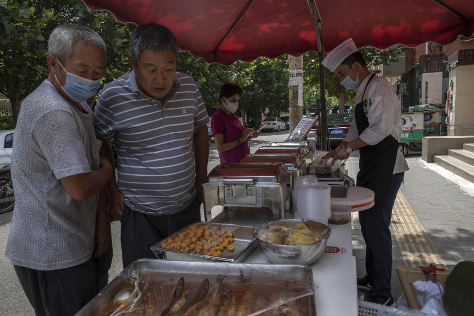 Residents some wearing masks to curb the spread of the coronavirus buy lunch at a restaurant that has started selling their food on the street to avoid the indoors in Beijing Wednesday, July 1, 2020. Three months after China declared victory over the coronavirus and started to reopen its economy, restaurants are among thousands of small businesses that are struggling to lure back skittish consumers nervous about the virus and possible job losses. (AP Photo/Ng Han Guan)