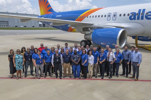 A group of employees pose in front of an Allegiant Air jet