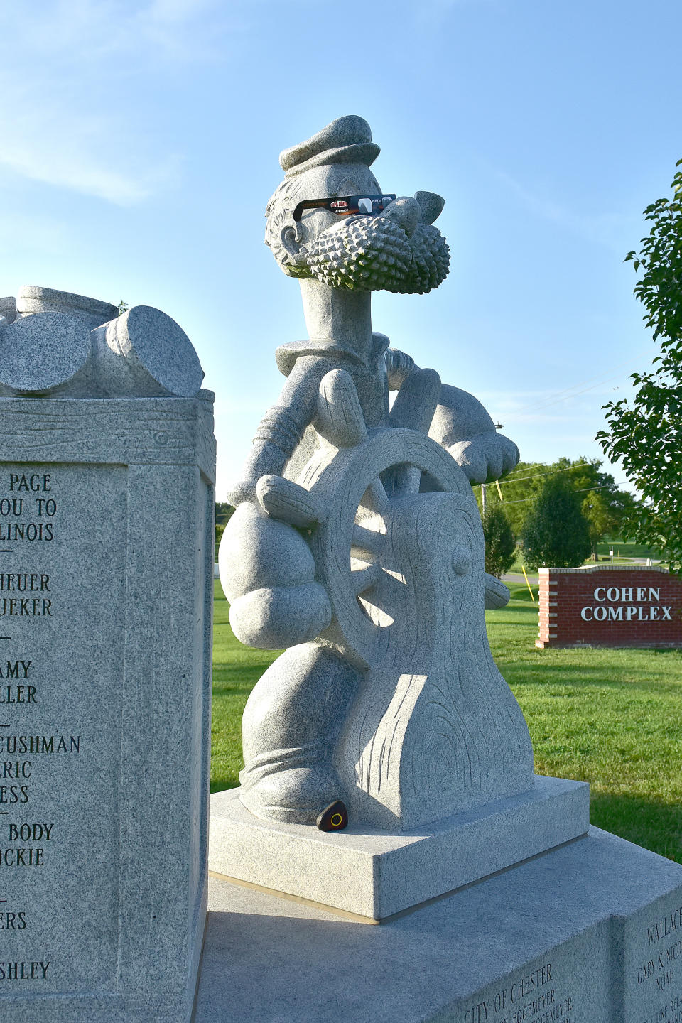 Statue of a sailor character from Popeye, possibly Popeye himself, standing on a ship's wheel