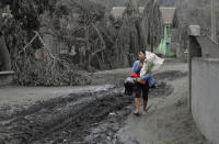 In this Tuesday, Jan. 14, 2020, photo, Leila de Castro carries a statue of the baby Jesus which she recovered from the house of her sister as she walks on a road covered with volcanic ash in Boso-Boso, Batangas province, southern Philippines. Taal volcano is spewing ash half a mile high and trembling with earthquakes constantly as thousands of people flee villages darkened and blanketed by heavy ash. (AP Photo/Aaron Favila)